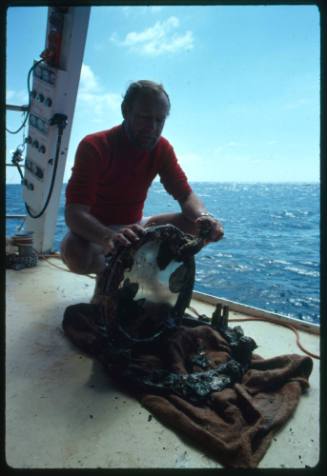 Marine Archaeologist Ron Coleman inspecting a porthole from a shipwreck on the deck of a vessel