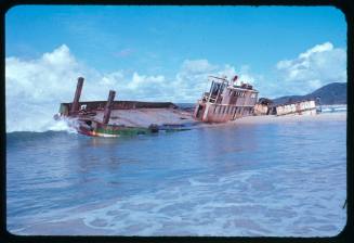 A shipwreck partially submerged underwater being hit by a wave