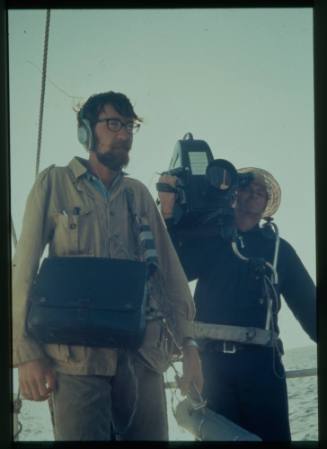 Shot of two people strapped in filming gear with ocean in background
