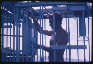 Ron Taylor standing inside a shark cage on board the Terrier VIII during the filming of the documentary Blue Water, White Death