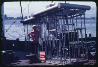 Valerie Taylor posing next to two shark cages on board the Terrier VIII