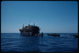 Three wooden rowboats following a wooden vessel