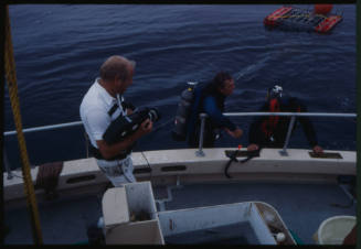 Person with camera and two divers at edge of boat