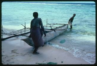 Two men taking outrigger canoe into water