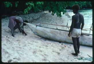 Two men with outrigger canoe pulled up on sand of beach