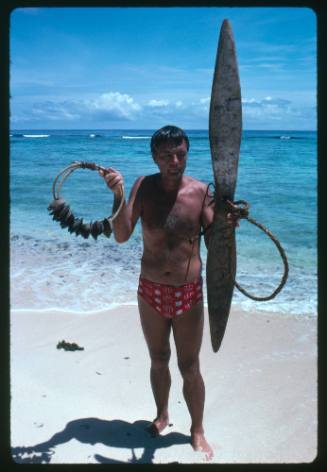 Ron Taylor standing on beach with shark calling object in each hand