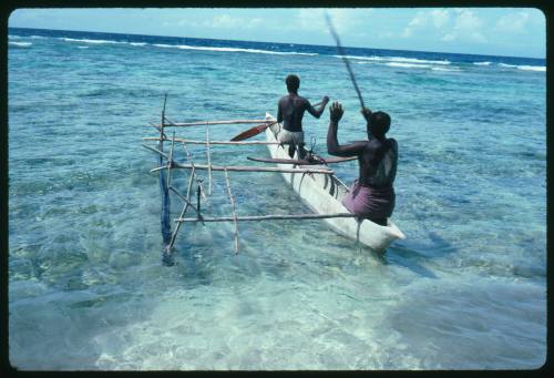 Two men paddling out to sea on outrigger canoe