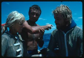 Ron Taylor showing a shark bite wound on his elbow to Valerie Taylor and one other person