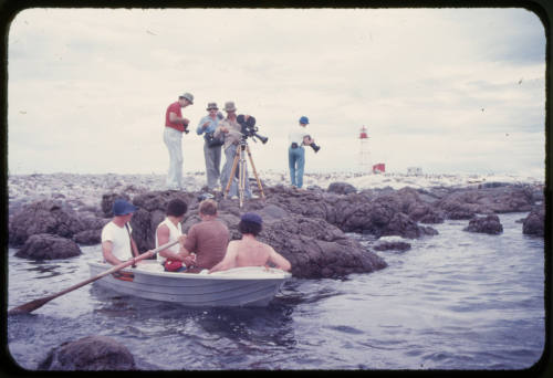 Men in dinghy and filming crew on rocky surface near water