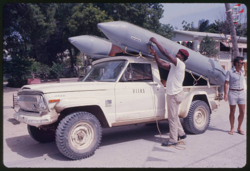 A man placing inflatable boat on back of a pick up truck and Ron Taylor