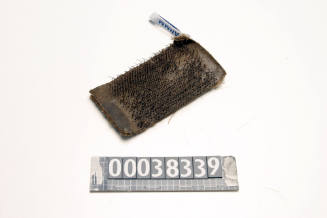 RECTANGULAR PIECE OF CARDBOARD COVERED BY THREE LAYERS OF CANVAS ON TOP, ON THE BOTTOM ARE MULTIPLE PIECES OF WIRE SIMULATING A BRUSH, USED TO CLEAN LEAD PARTS