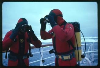 Two men in red diving suits putting mask on