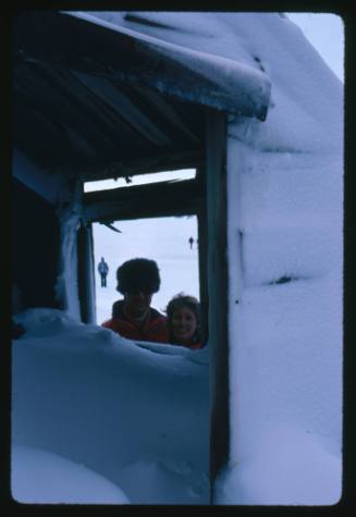 Two people smiling at the camera through a window