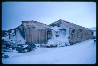 Two wooden buildings partially covered in snow