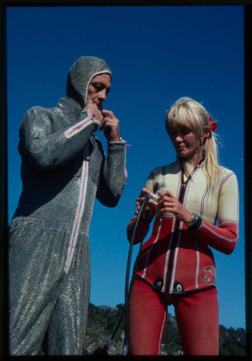 Ron Taylor in the chainmail suit (mesh suit) next to Valerie Taylor in a west suit testing out diving equipment