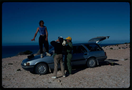 Man standing on the hood of a car talking with two others