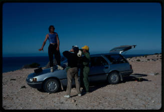 Man standing on the hood of a car talking with two others