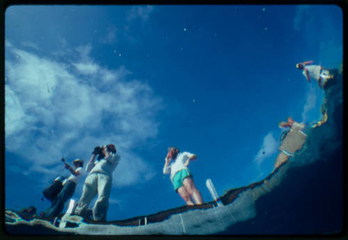 Photograph shot from underwater of a film crew at the water's edge