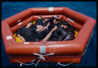 Actors lying with dummy corpses in a hexagonal inflatable raft