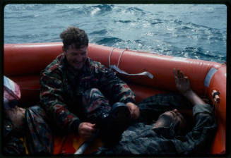 Actor sitting with dummy corpses in a hexagonal inflatable raft