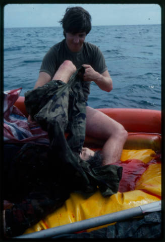 Actor putting on pants next to a dummy corpse in an inflatable raft