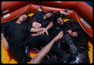 Actors lying with dummy corpses in a hexagonal inflatable raft