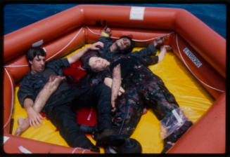 Actor lying with dummy corpses in a hexagonal inflatable raft