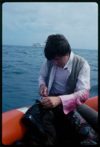 Man sitting in a raft cutting a boot with a knife