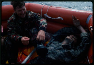 Actor lacing his boot next to a dummy corpse in an inflatable raft