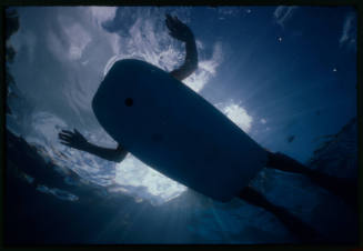 Underwater silhouette of a person with limbs splayed on a bodyboard