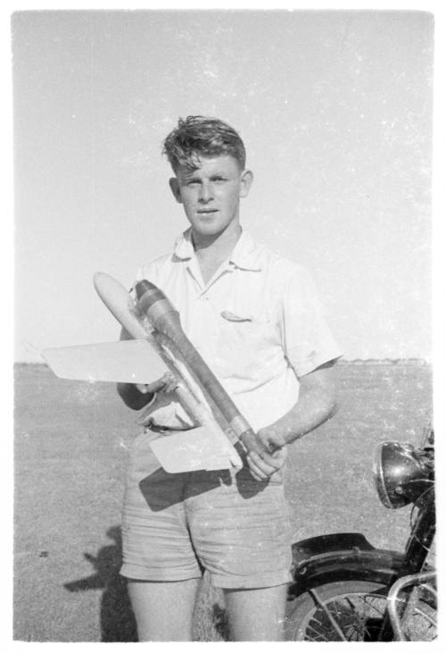 Young man standing in front of a bike holding a model plane