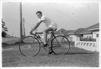 Man posing on a bicycle in front of some houses