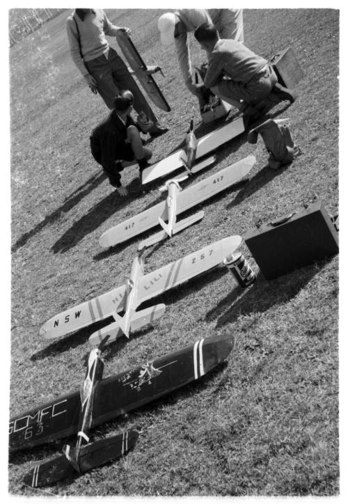 Four people in a grassy field inspecting a line of model planes 