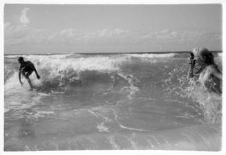 Black and white photo of Valerie Taylor standing in the water taking a photo of a surfer