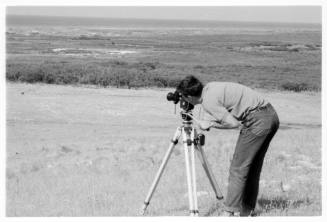 Black and white photo of a man with a tripod camera shooting the landscape