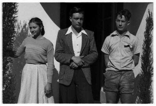 Black and white photo of a young woman and two young men standing in front of a building door