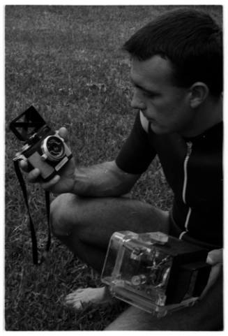 Black and white photo of Ron Taylor crouched while holding two cameras