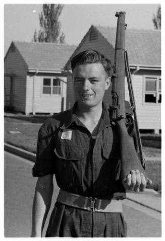 Black and white photo of a young Ron Taylor dressed in uniform posing with a rifle