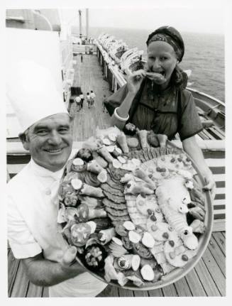 Photograph depicting a chef with a food platter and a woman