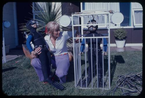 Valerie Taylor next to a mini shark cage prop and dummy divers