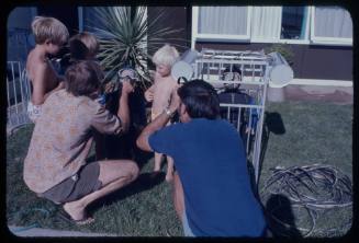 A man showing a mini dummy diver and model shark cage to three children while another man films. 