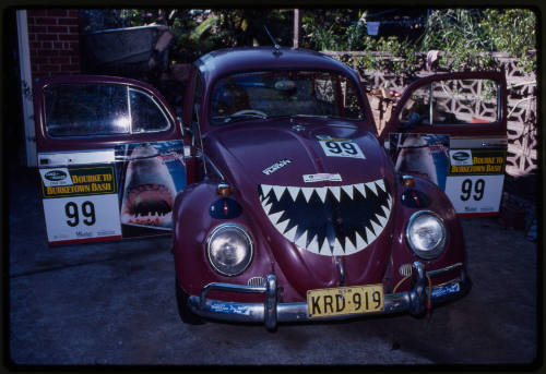 Front on shot of maroon Volkswagen Beetle with shark-related stickers on it, including cartoon shark jaw on front hood