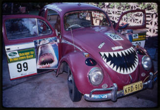 Maroon Volkswagen Beetle with shark-related stickers on it, including cartoon shark jaw on front hood