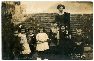 Photographic postcard of a female teacher with her kindergarten class at Miss Capon's Private School in Portsmouth, United Kingdom