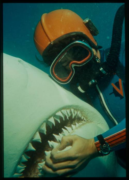 Underwater close up shot of a scuba diver wearing helmet holding the jaw of a shark