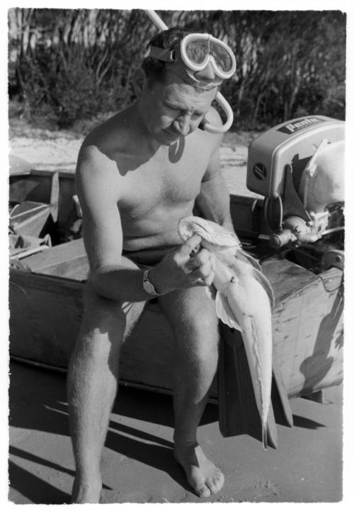 Shot of diver holding a caught fish while sitting on the edge of a dinghy