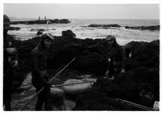 Shot of spearfishers on rocky platform by ocean