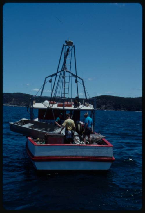 Fishing boat at sea with three people on board and dinghy on deck