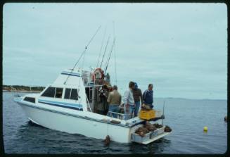 Side view of fishing boat at sea with five people on board at stern