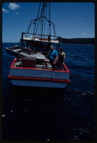 Fishing boat at sea with three people on board and dinghy on deck